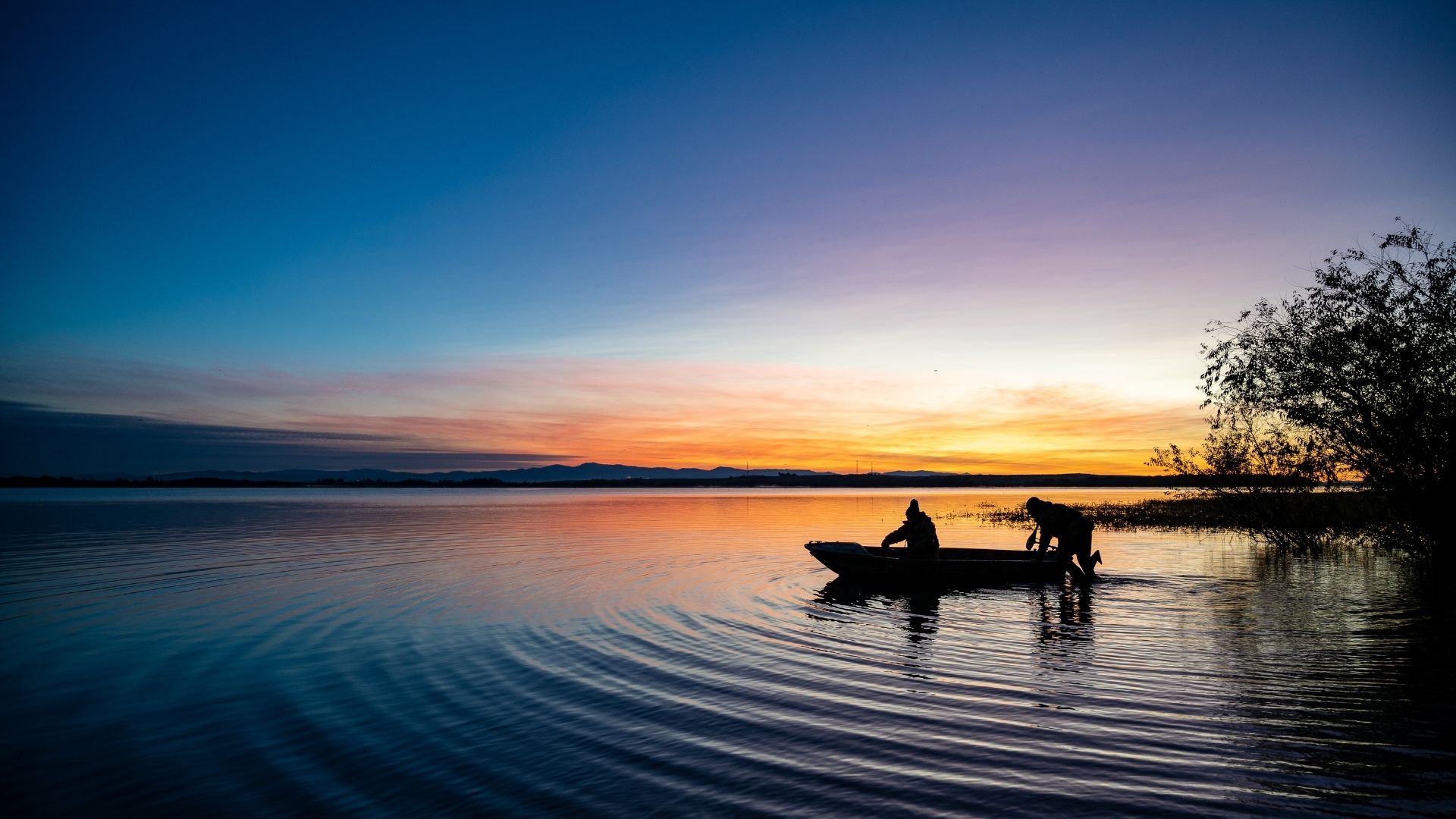 Two anglers in a boat on a river at sunset